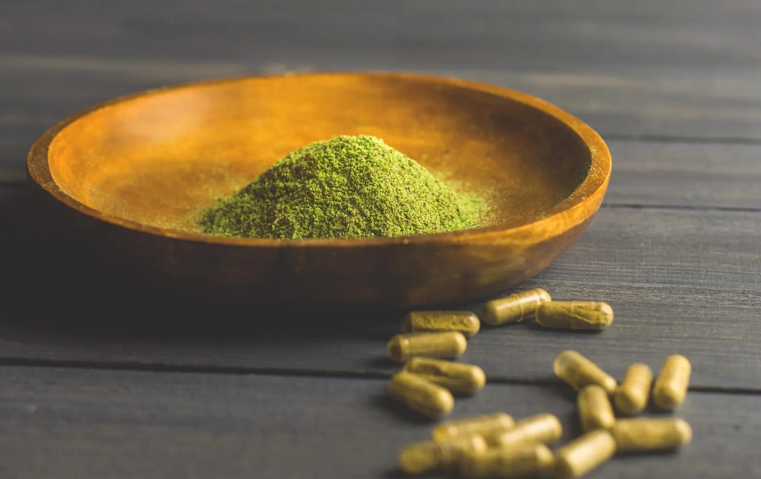 a bowl of green powder and capsules