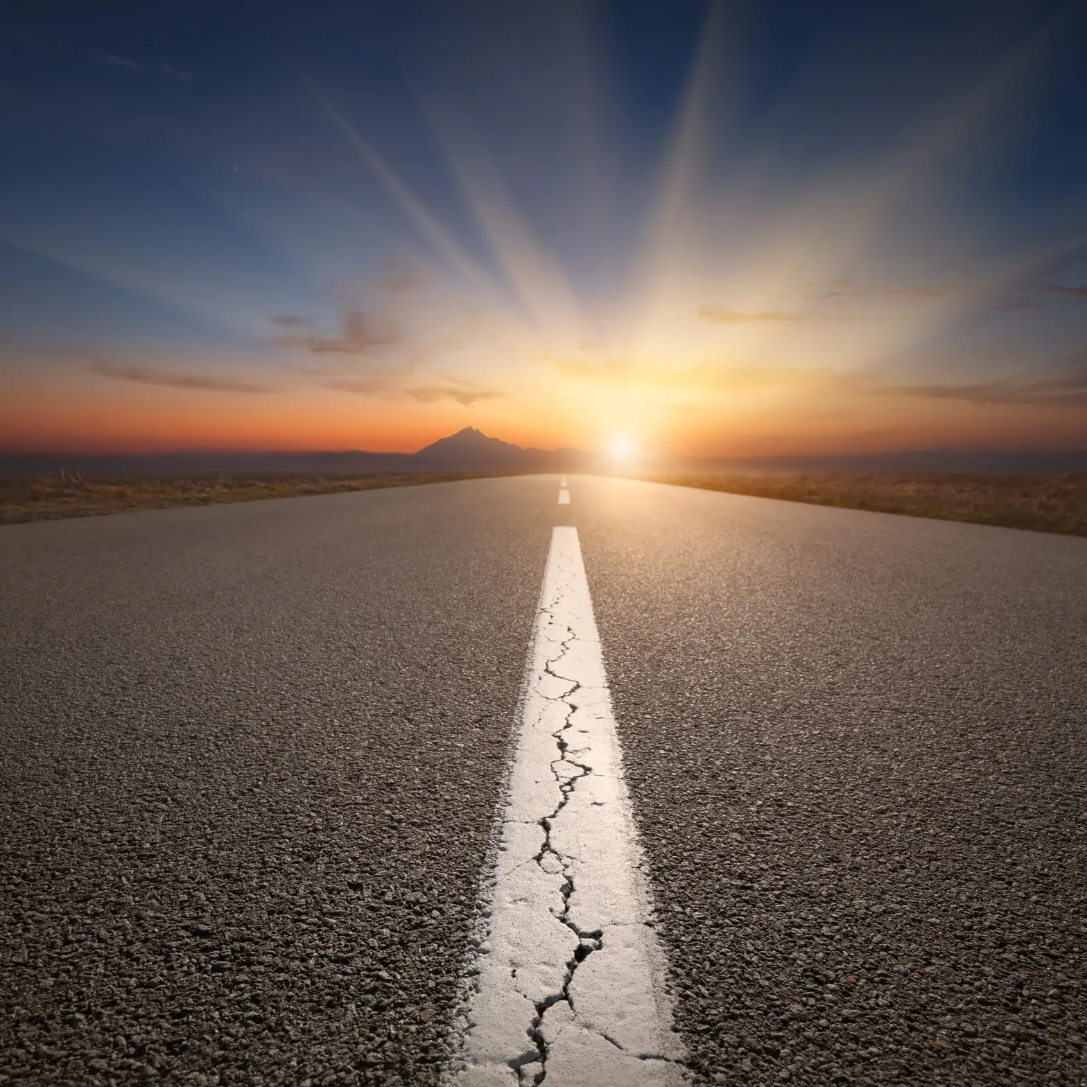 Empty highway leading to the mountains through the desert against the rising sun with big sunbeams at beautiful sunrise. Success concept The Benefits of Traveling Out of the State for Addiction Treatment