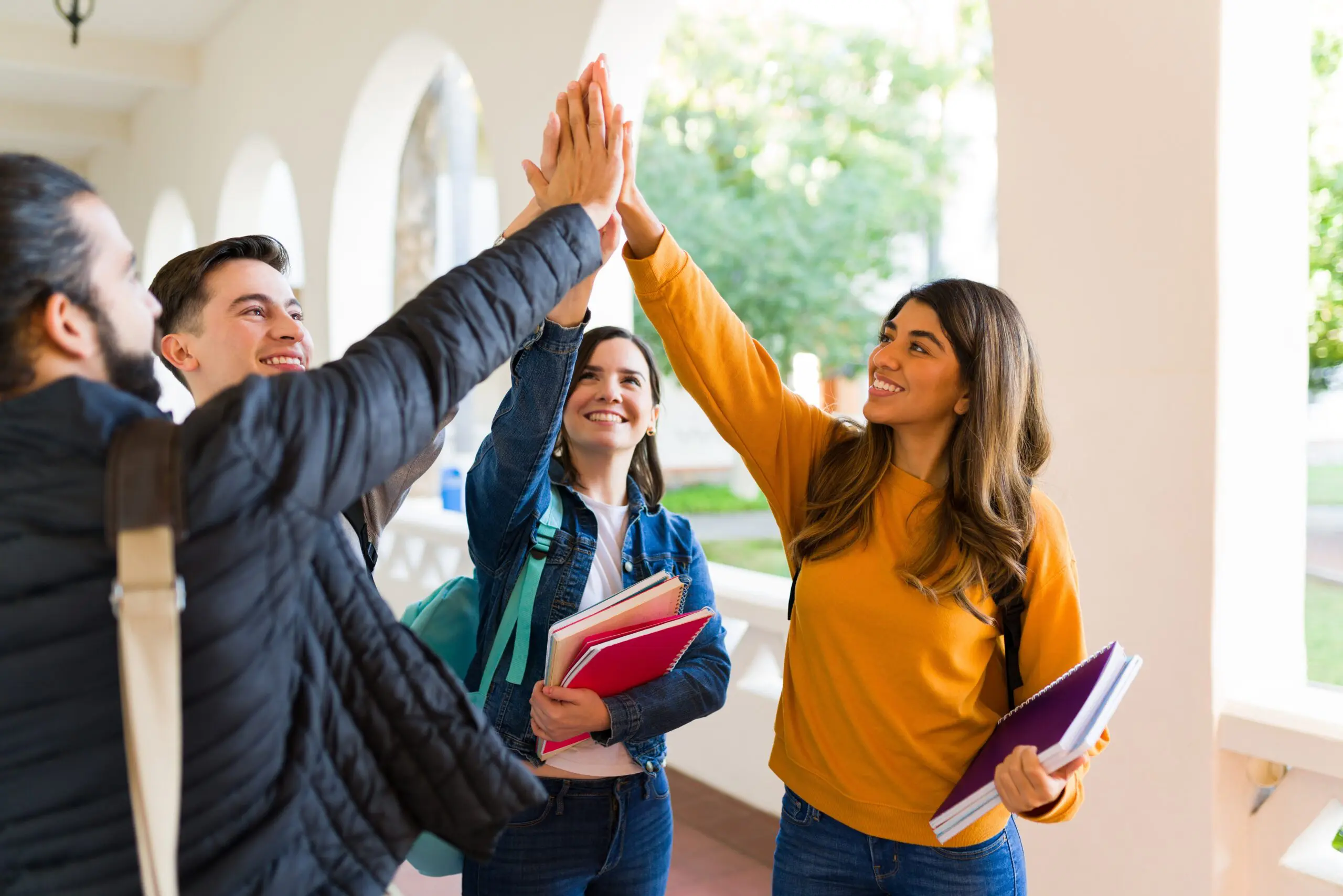 Cheerful students laughing and giving a high fives after finishing their college exams and homework