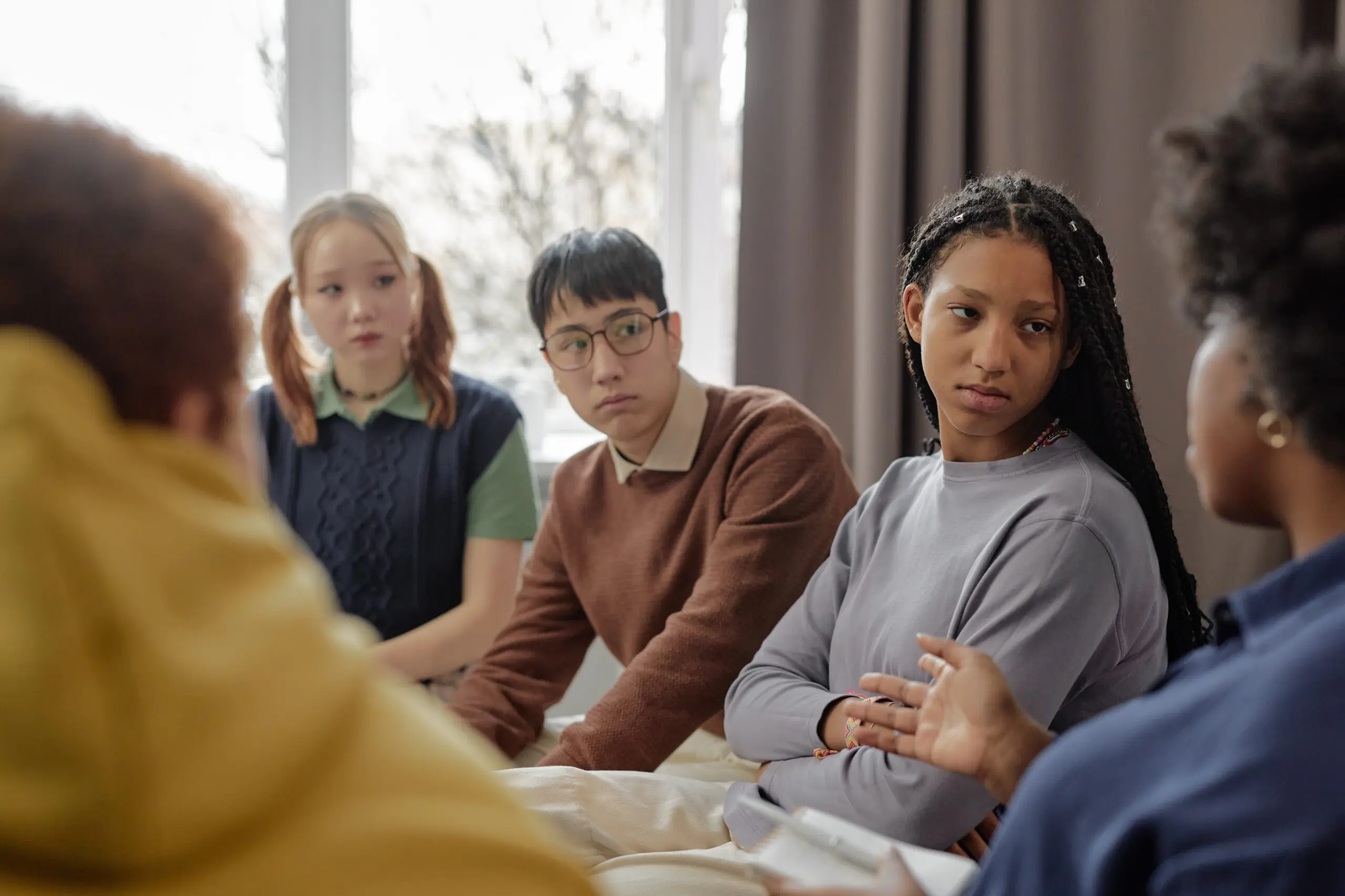 Multiethnic group of teenage children listening to female therapist during support session in school or community center scaled How to Make It Through School