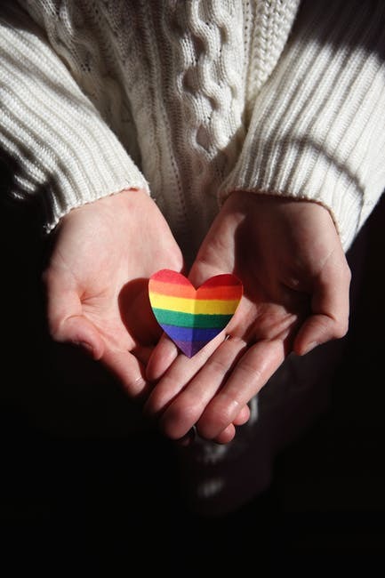 A woman holding an LGBTQ+ heart in her hands
