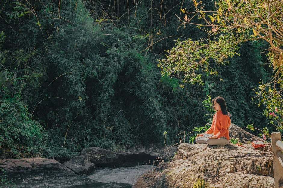 a woman sitting next to a creek as part of a holistic approach to wellness from addiction