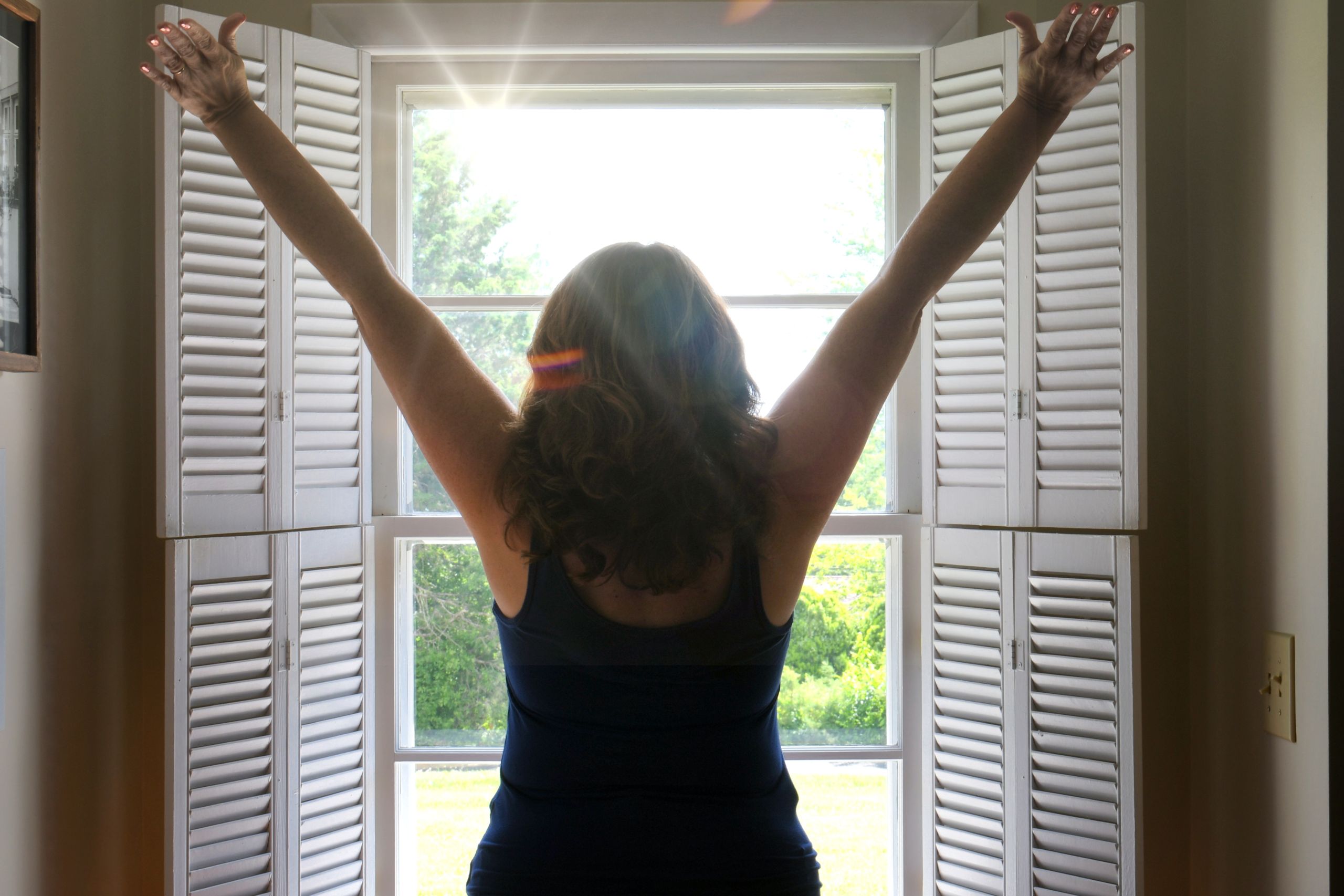 Morning looking out her window at sunrise feeling refreshed with her hands in the air