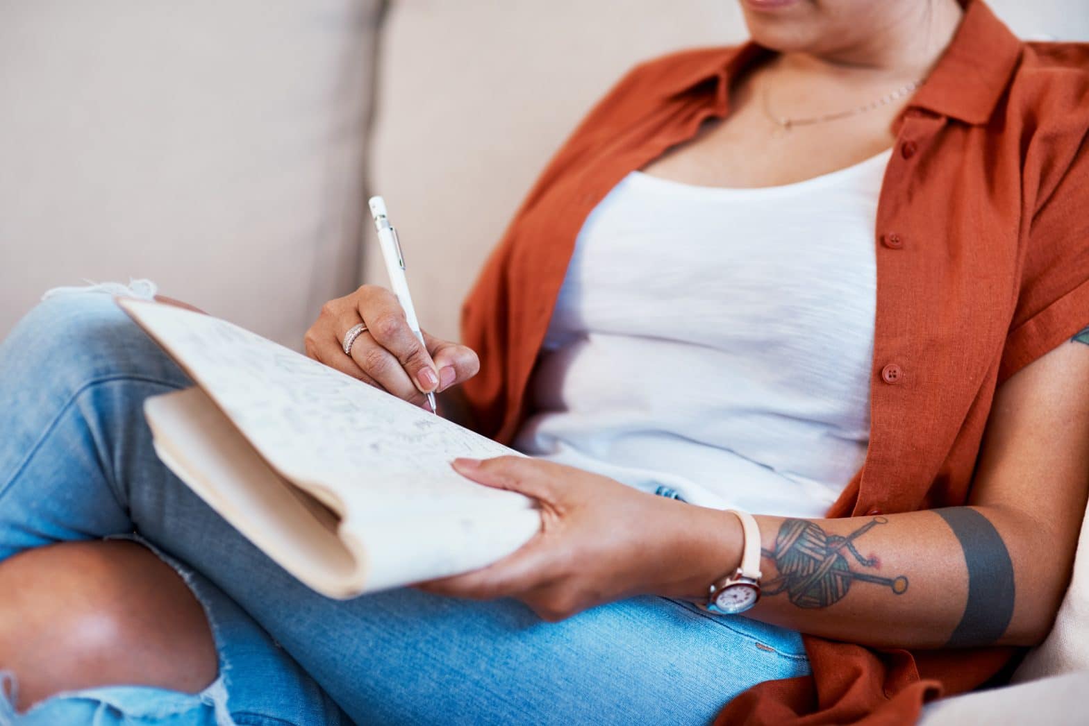 a woman sitting on a couch writing on a piece of paper