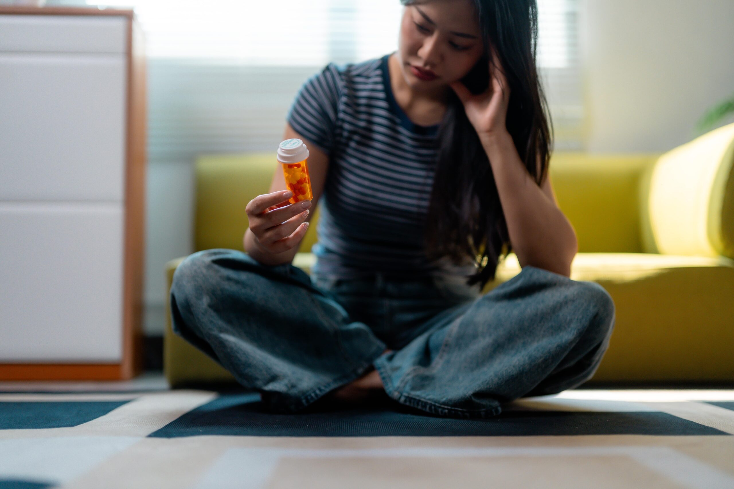 Asian woman sitting on the floor at home looking at a pill bottle scaled Can Xanax Make Anxiety Worse?