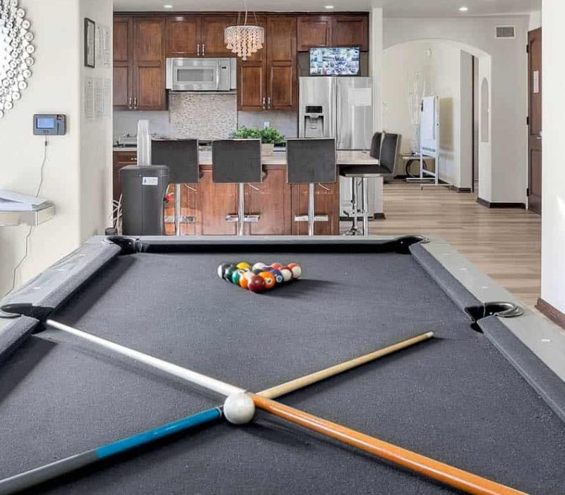 a pool table with cue sticks and balls in a room with a kitchen