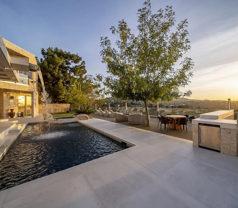 a pool and a house with a tree and a sunset