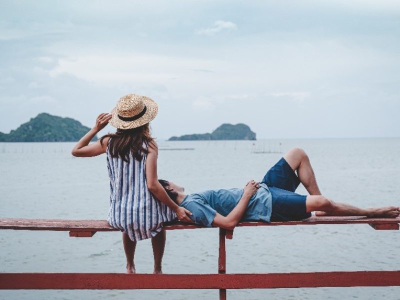 a man and woman sitting on a railing by water